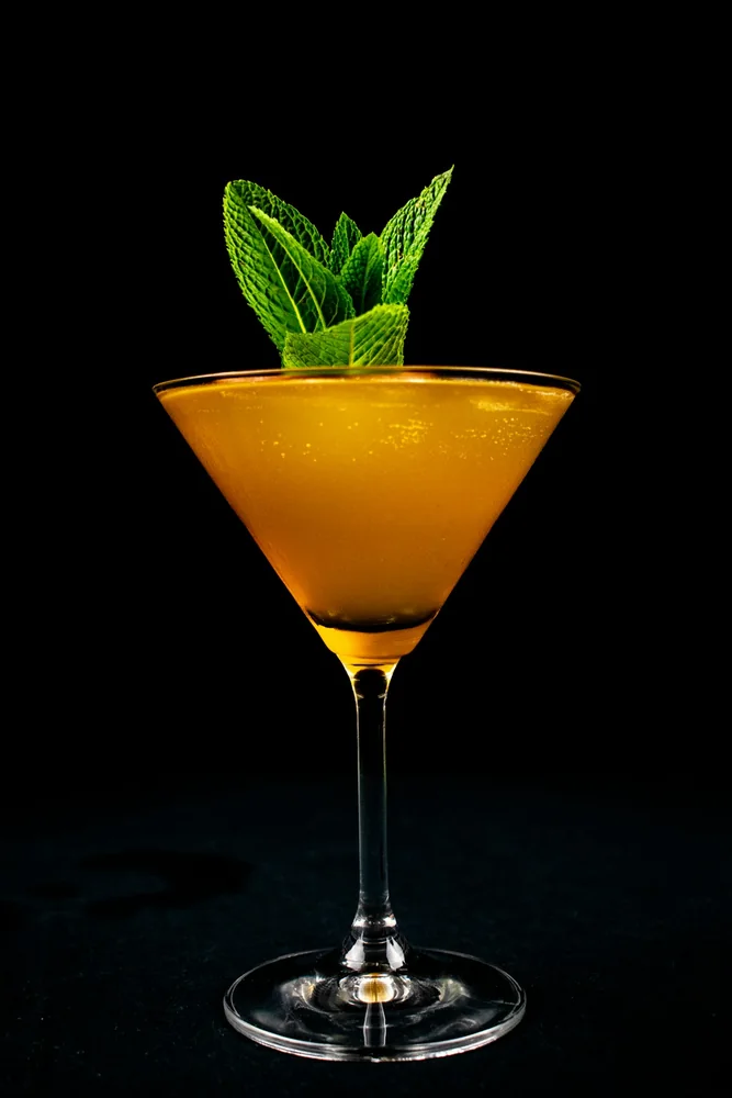 A golden cocktail photographed with a fresh mint garnish